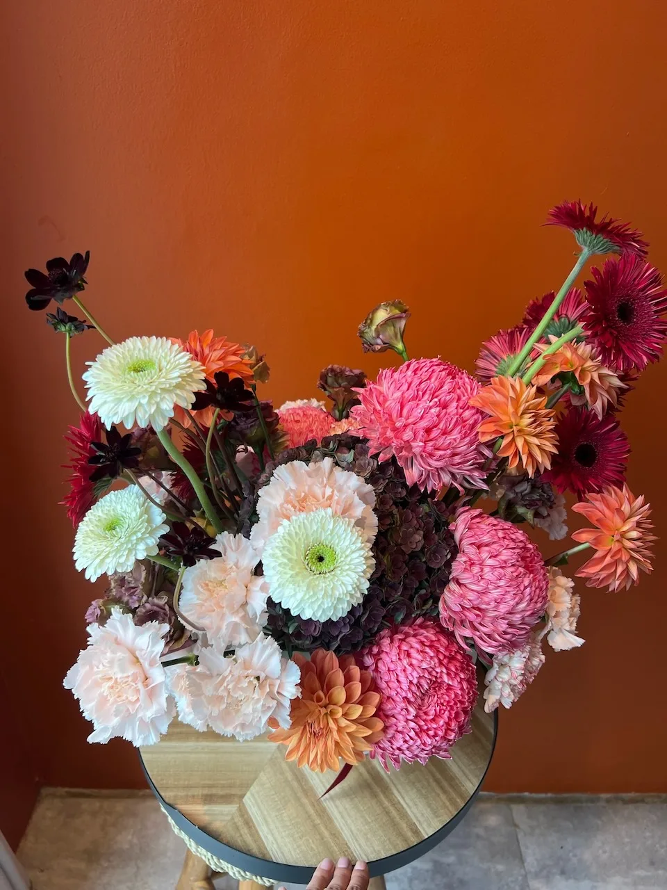 Lush arrangement of coral, pink and cream dahlias with burgundy cosmos on a wooden stool