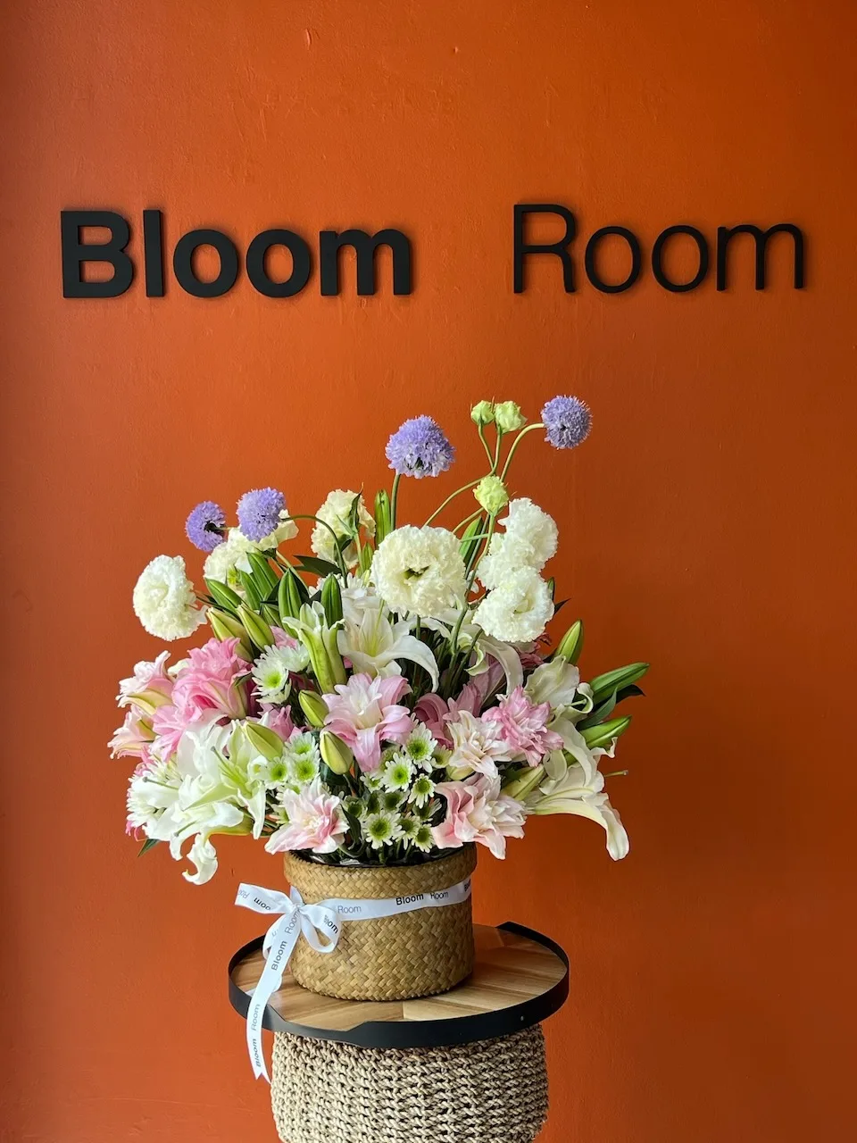 Mixed arrangement in a woven wicker basket with white lilies, pink chrysanthemums, white lisianthus and purple allium