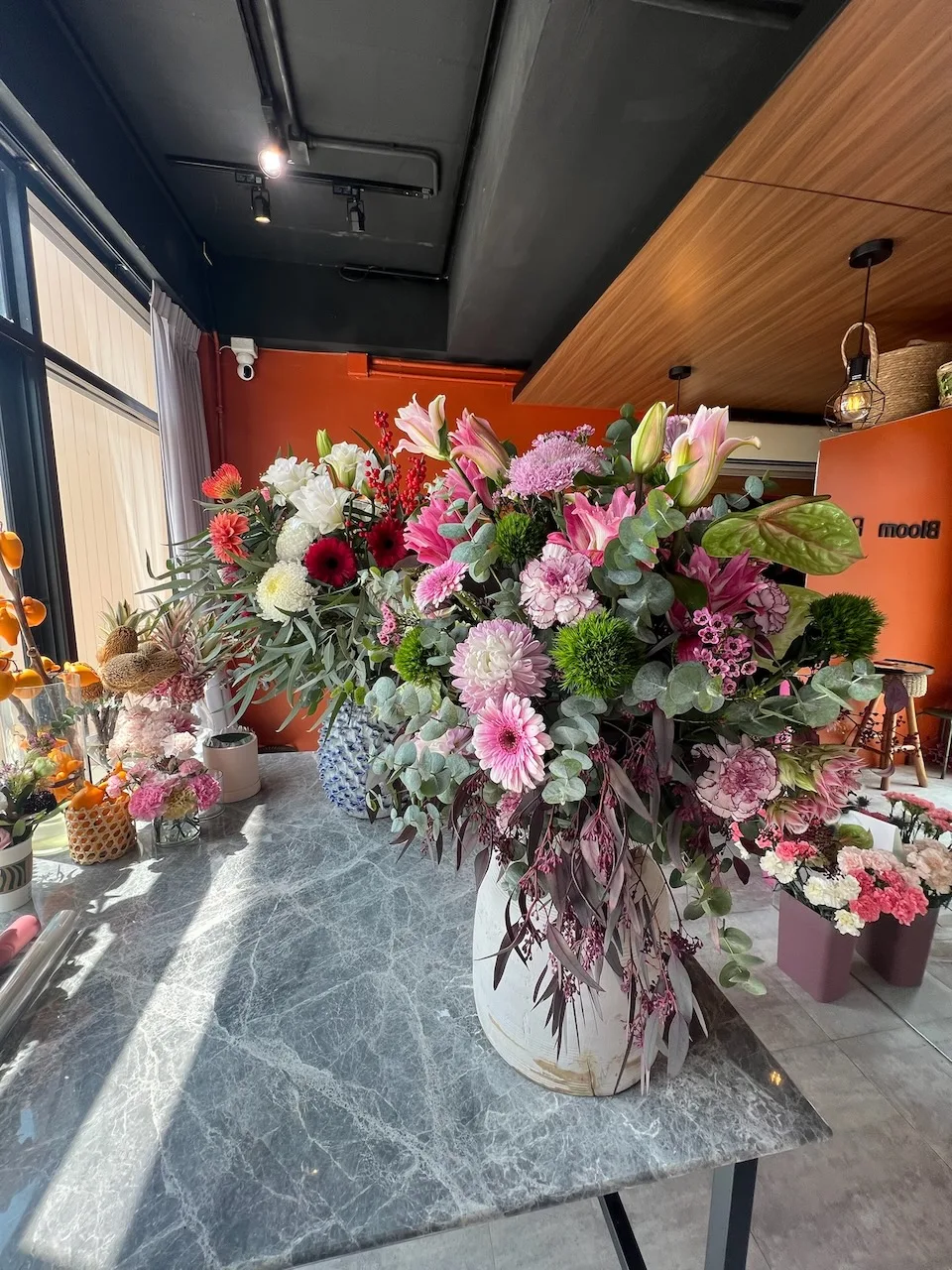 Oversize arrangement of pink lilies, pink gerberas, green chrysanthemums, lavender mums and eucalyptus in a white ceramic vase