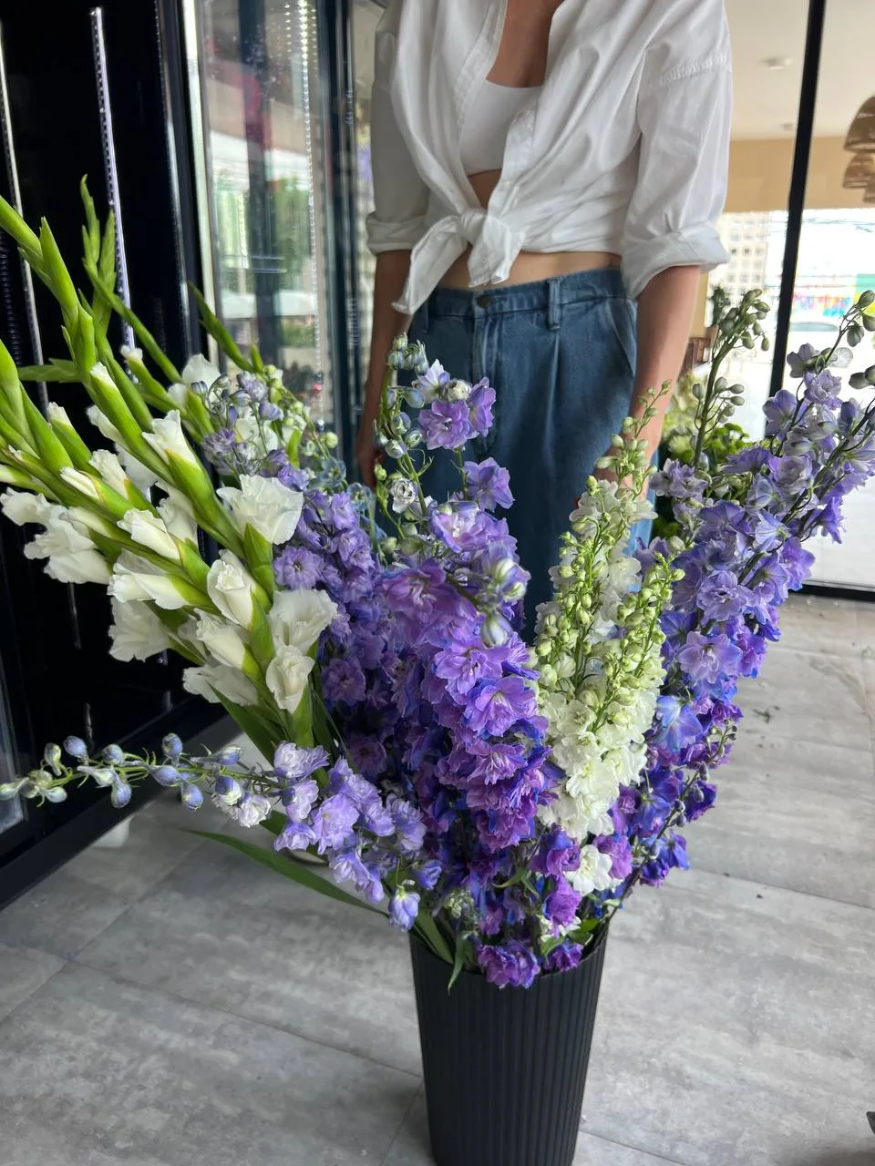 Tall arrangement of purple delphinium and white lisianthus in a ridged dark vase