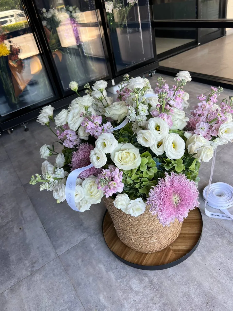 White lisianthus and pink pompom basket placed outside the storefront