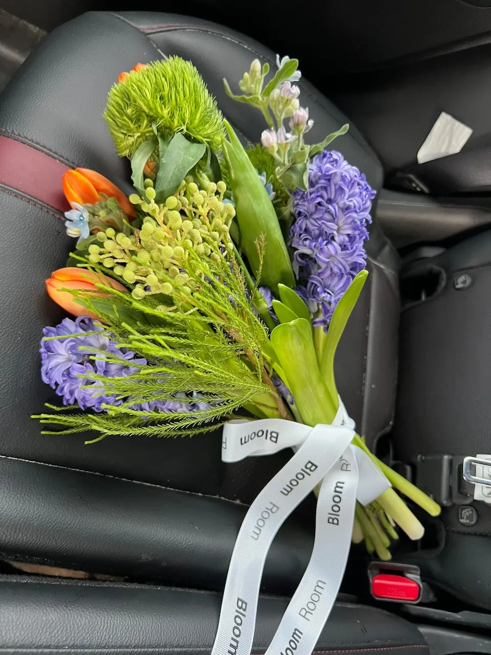 Small bouquet of purple hyacinth, orange tulips and greens on a car seat ready for delivery