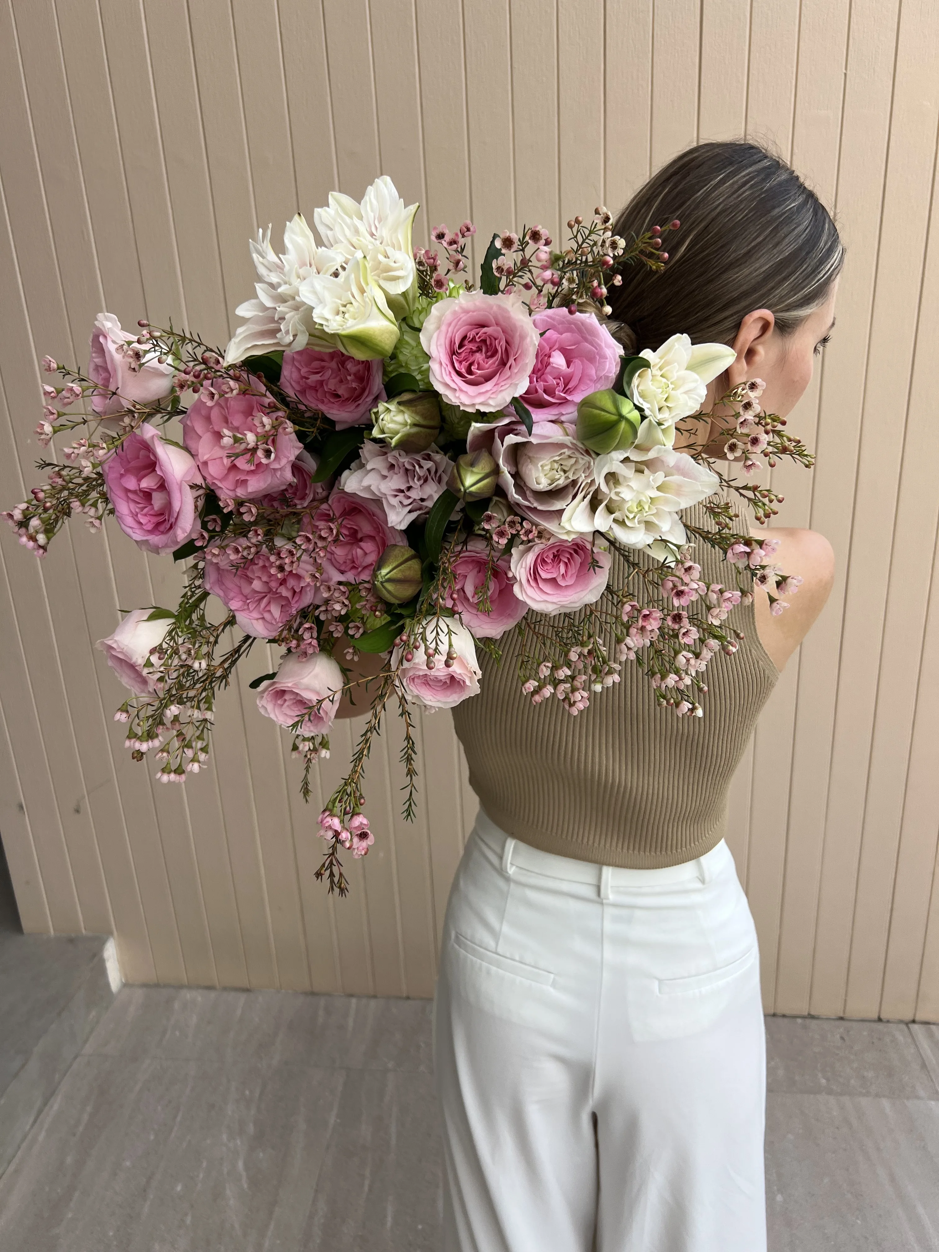 Back view of a woman holding a lush pink garden rose and wax flower bouquet