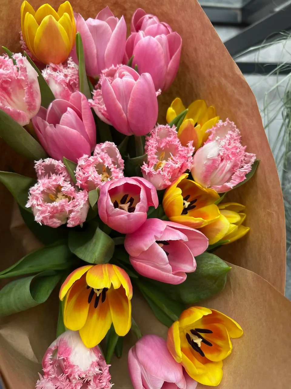 Kraft-wrapped bouquet of pink, yellow and fringed tulips from a flat-lay angle