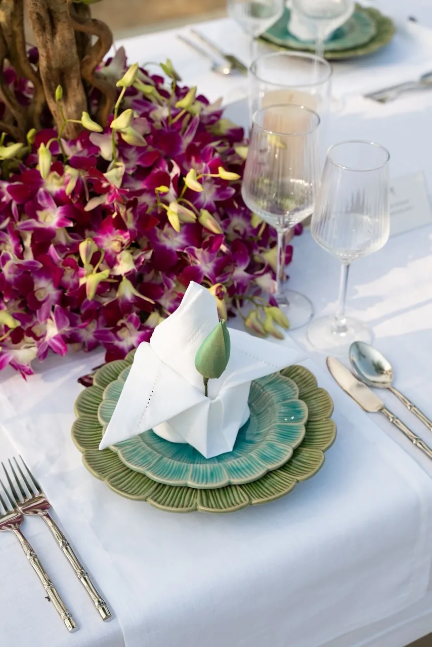 Elegant table setting with orchid centerpiece, ceramic charger plates and lotus bud napkin