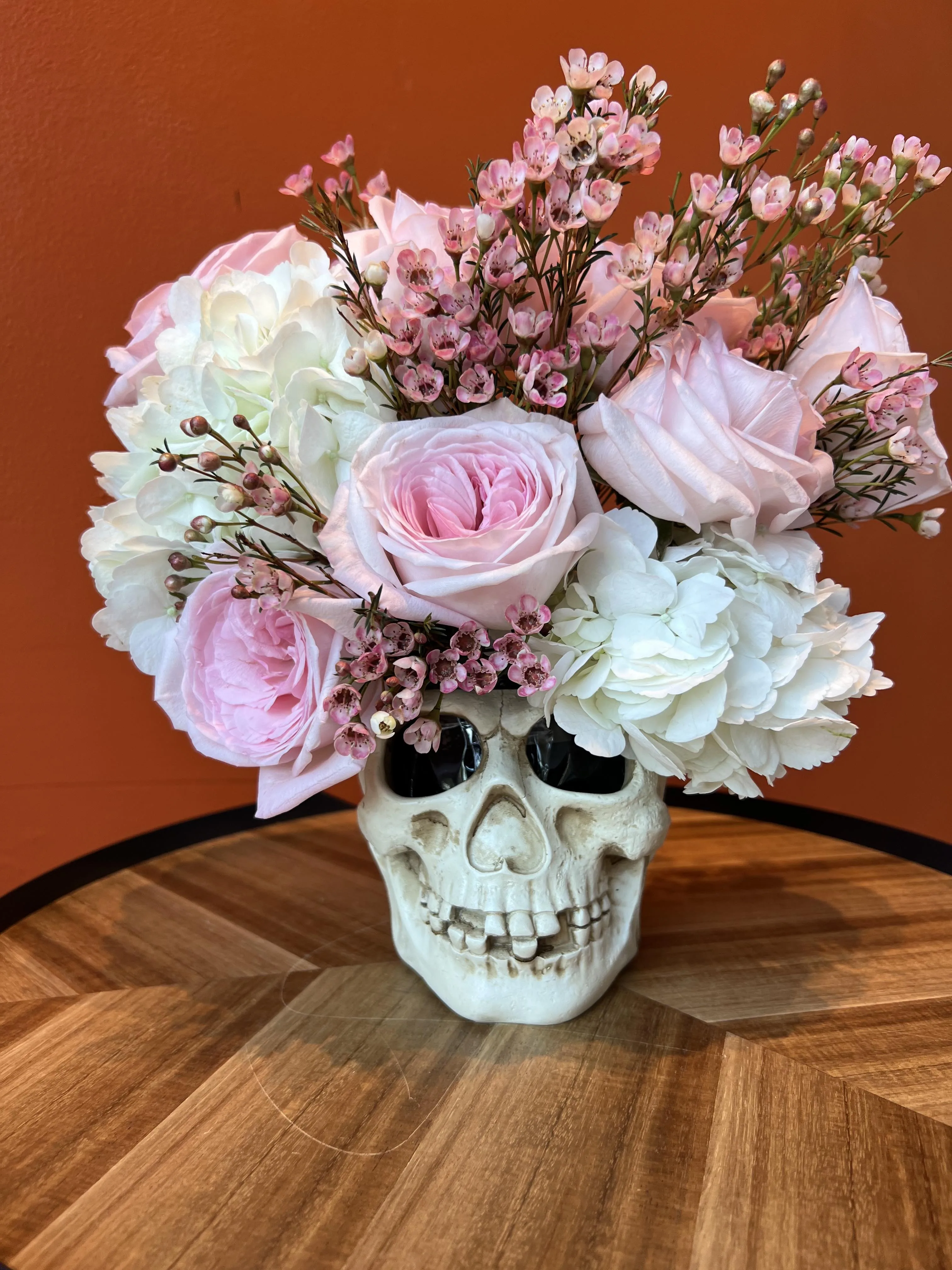 Pink garden roses and wax flower arranged in a white ceramic skull for a Halloween shoot