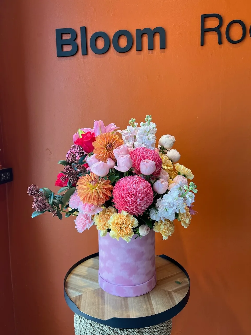 Lush pink hatbox with chrysanthemums, orange dahlias, white stock and yellow carnations