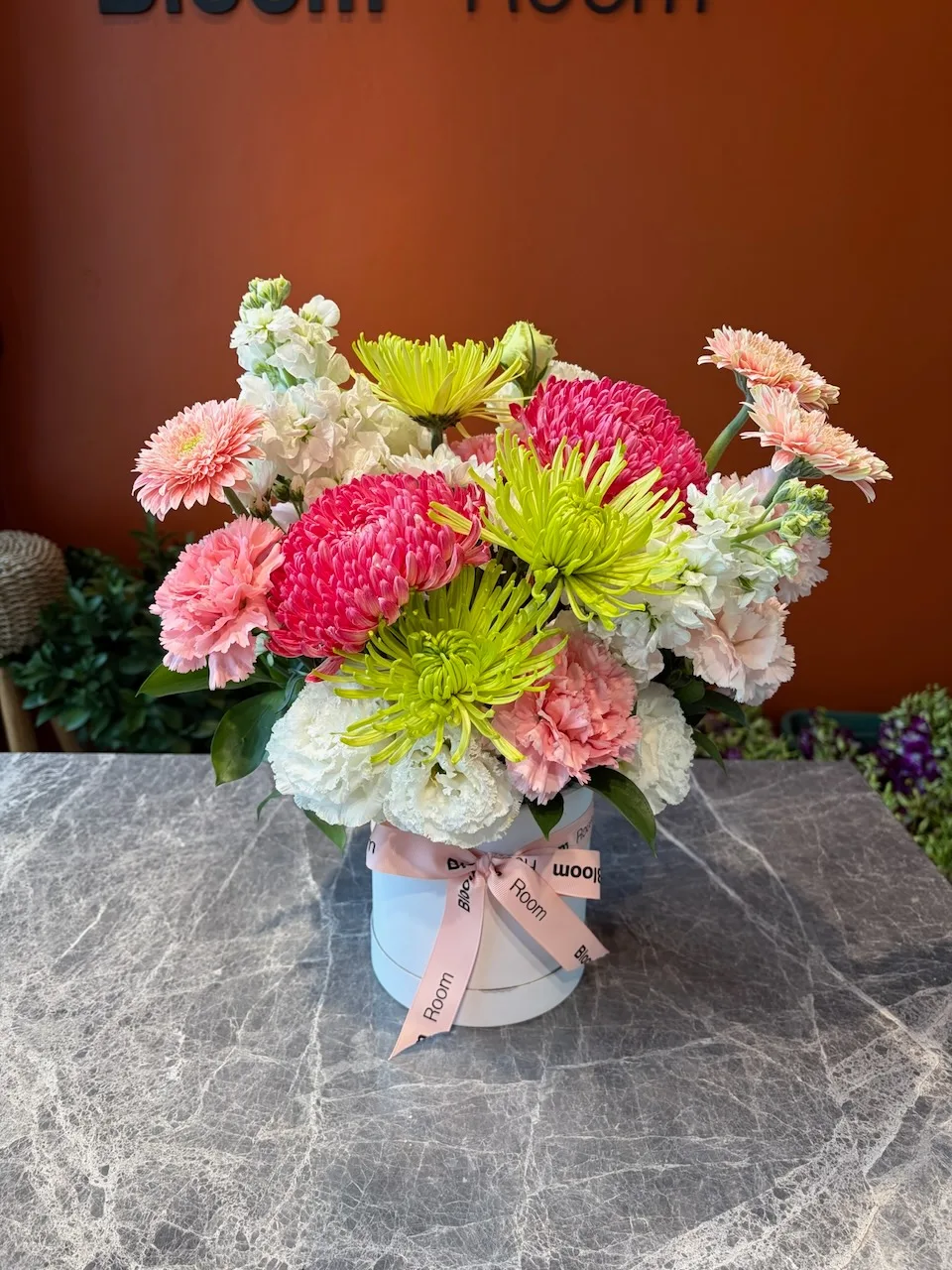 Pink and green dahlia arrangement with chrysanthemums in a small blue hat box on marble