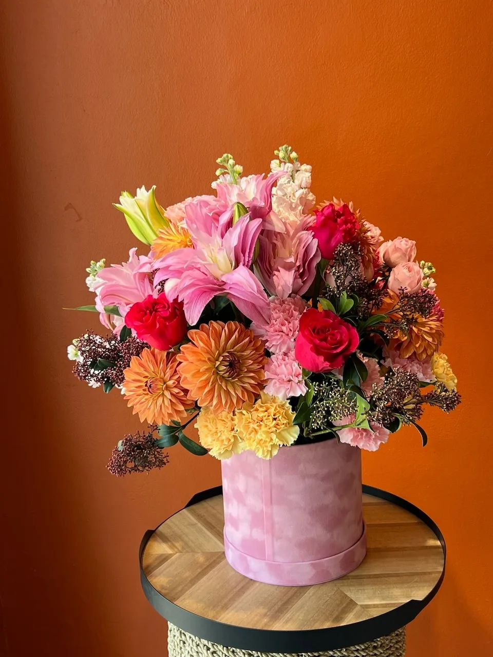 Vibrant pink hatbox with oriental lilies, orange dahlias, red roses and white snapdragons