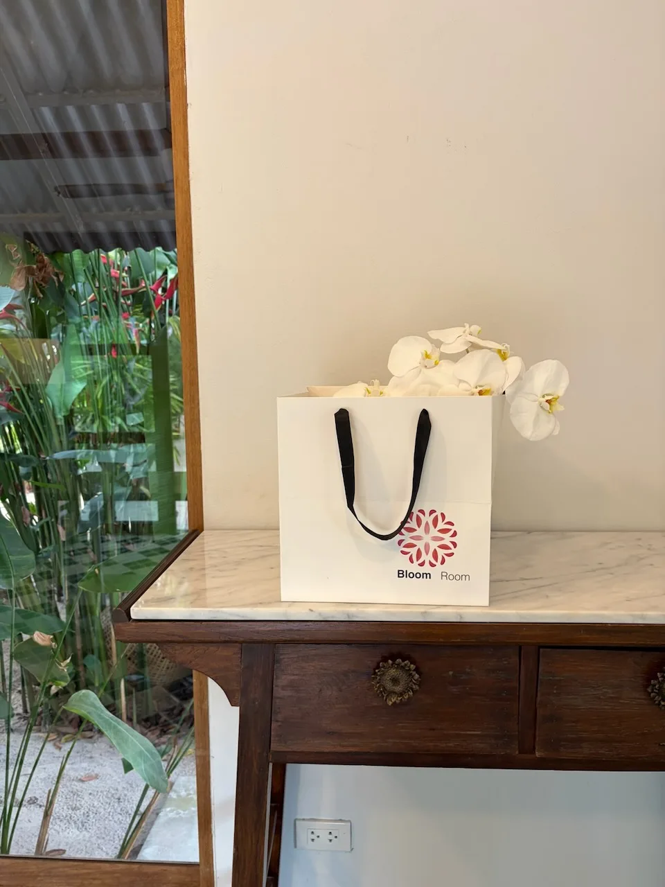 White phalaenopsis orchids arranged in a Bloom Room gift bag on a wooden console by a window