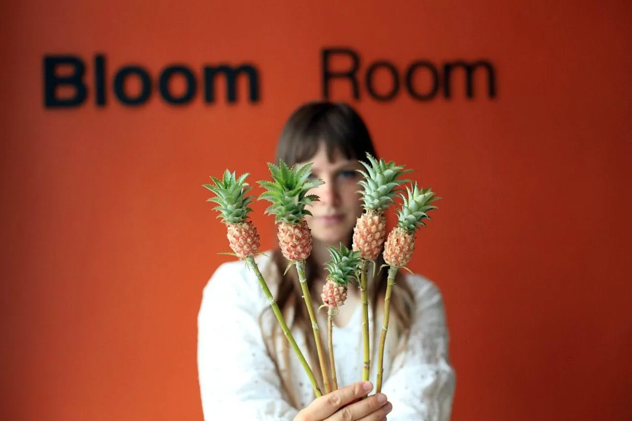 ผู้หญิงถือช่อสับปะรดประดับด้านหน้าป้าย Bloom Room สีส้ม